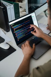 Close-up of a programmer pointing at a colorful code script on a laptop in a business office setting.