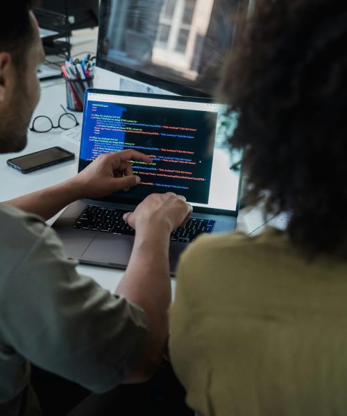 Two adults collaborating on programming tasks using a laptop in an office setting. showcasing modern business technology solutions